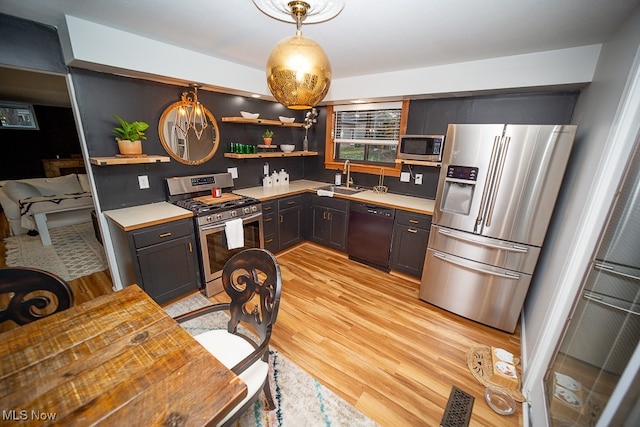 kitchen featuring appliances with stainless steel finishes, light hardwood / wood-style flooring, hanging light fixtures, and sink