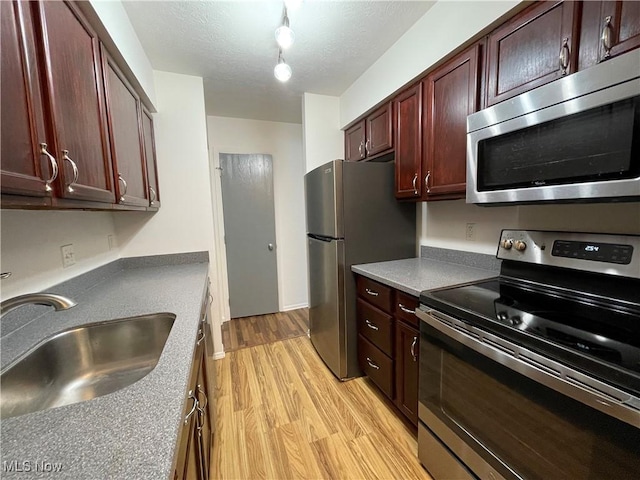 kitchen featuring sink, stainless steel appliances, light hardwood / wood-style flooring, a textured ceiling, and track lighting