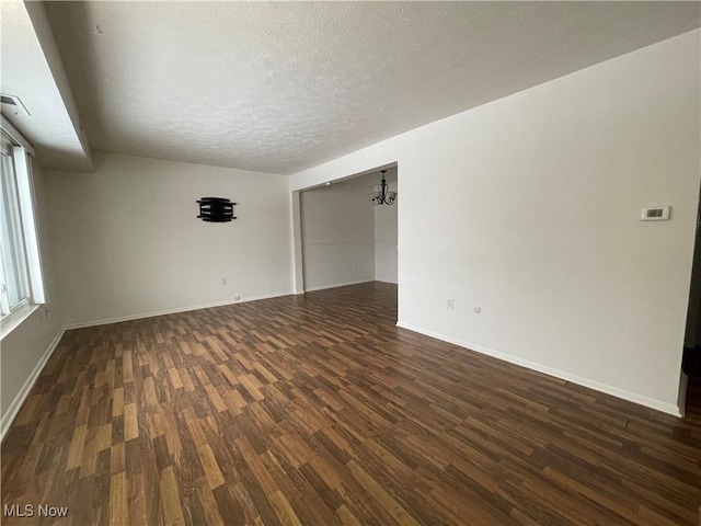 empty room featuring dark hardwood / wood-style floors, a textured ceiling, and a chandelier