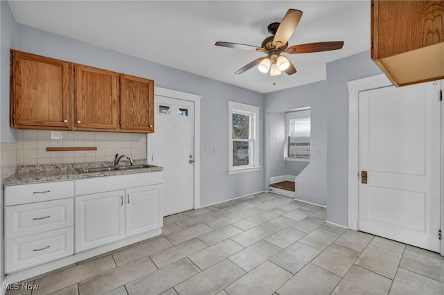 kitchen with ceiling fan, sink, tasteful backsplash, light stone counters, and white cabinets