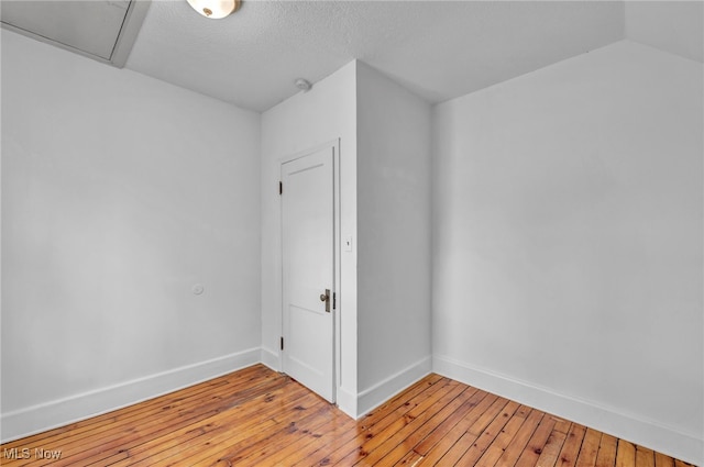 spare room featuring vaulted ceiling, a textured ceiling, and light hardwood / wood-style flooring