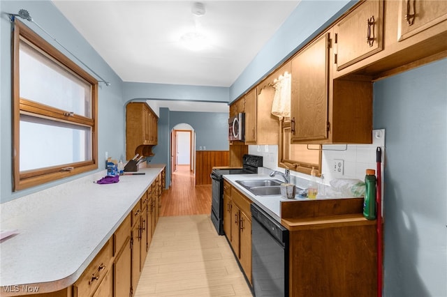 kitchen featuring wood walls, backsplash, black appliances, sink, and light hardwood / wood-style flooring