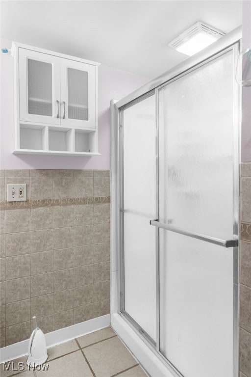 bathroom with tile patterned flooring, a shower with shower door, and tile walls