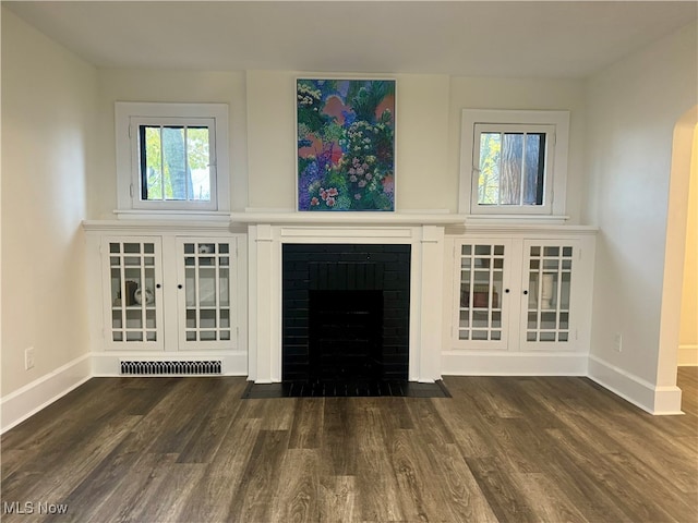 unfurnished living room featuring a fireplace, dark wood-type flooring, and a healthy amount of sunlight