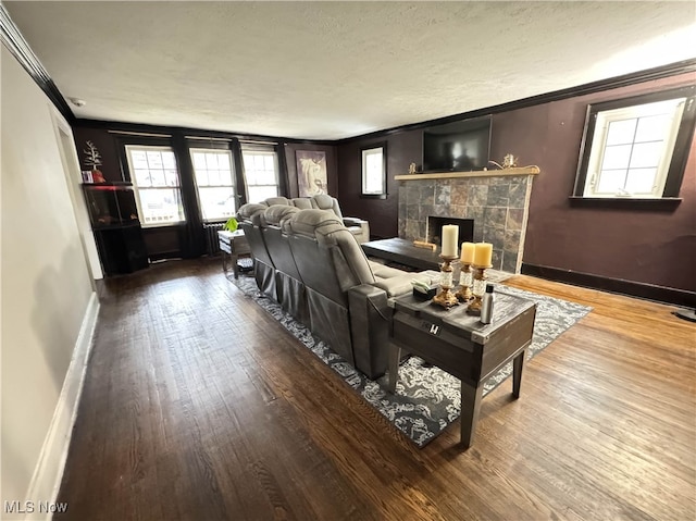 living room with a tile fireplace, ornamental molding, a textured ceiling, and hardwood / wood-style flooring