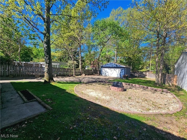 view of yard with a garage, a fire pit, a fenced backyard, and an outbuilding
