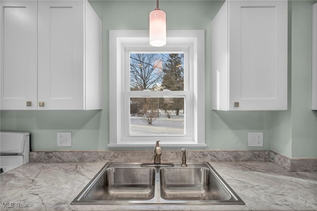 kitchen with light stone counters, white cabinetry, and sink