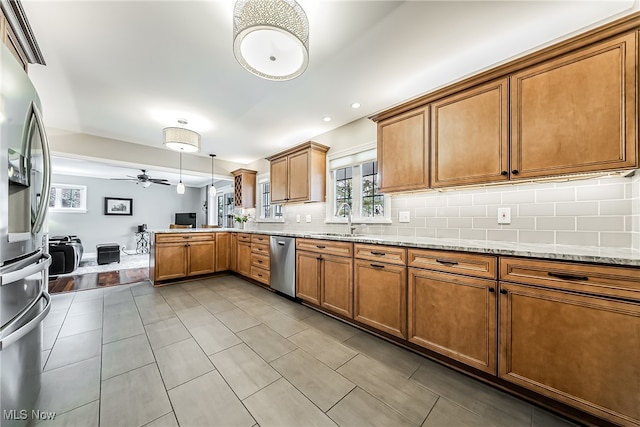 kitchen with appliances with stainless steel finishes, light stone counters, ceiling fan, sink, and pendant lighting