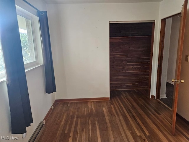 unfurnished bedroom with a baseboard heating unit, a closet, and dark wood-type flooring