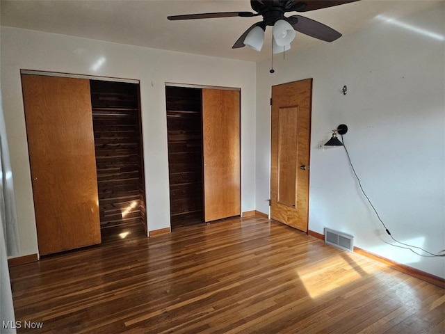 unfurnished bedroom featuring hardwood / wood-style flooring, ceiling fan, and two closets