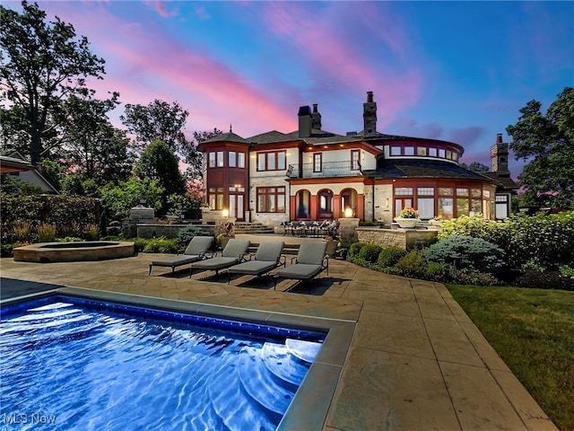 back house at dusk featuring a swimming pool with hot tub and a patio