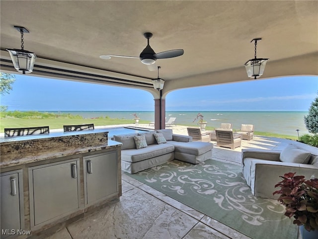 view of patio featuring outdoor lounge area, ceiling fan, exterior kitchen, a view of the beach, and a water view