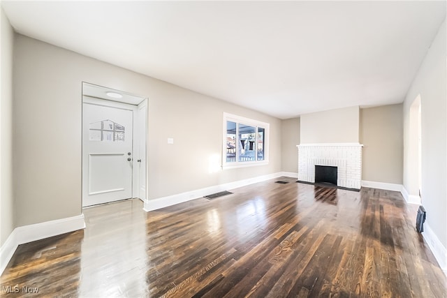 unfurnished living room featuring dark hardwood / wood-style flooring and a brick fireplace