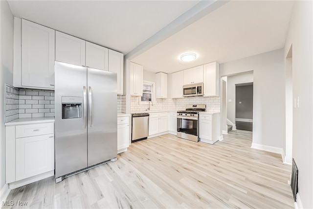 kitchen featuring light wood-type flooring, stainless steel appliances, white cabinetry, and backsplash