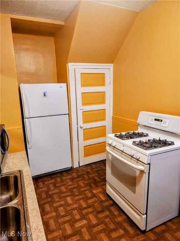 kitchen with a textured ceiling, white appliances, vaulted ceiling, and dark parquet flooring