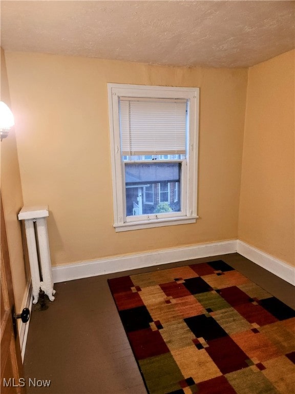 unfurnished room with dark colored carpet, a textured ceiling, and radiator