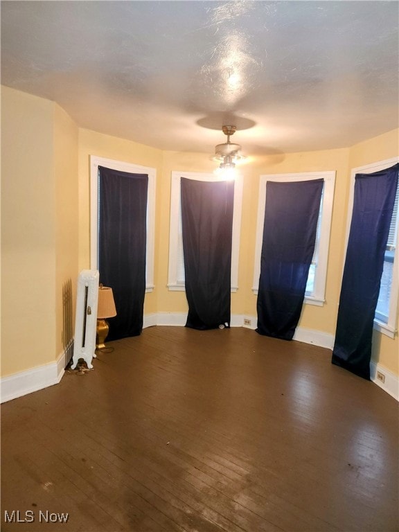 spare room with radiator heating unit, ceiling fan, and dark wood-type flooring