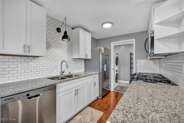 kitchen featuring hardwood / wood-style floors, white cabinets, sink, stacked washer / drying machine, and stainless steel appliances