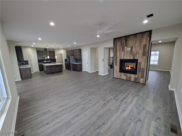 unfurnished living room featuring hardwood / wood-style floors, ceiling fan, and a large fireplace