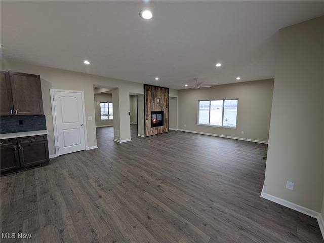 unfurnished living room with ceiling fan, a large fireplace, and dark wood-type flooring