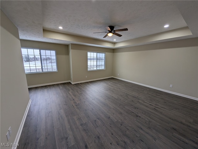 empty room with a textured ceiling, a tray ceiling, ceiling fan, and dark wood-type flooring