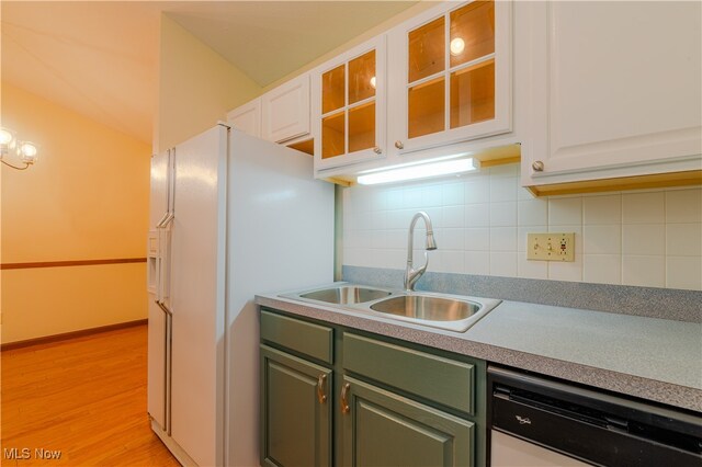 kitchen featuring dishwashing machine, white refrigerator with ice dispenser, a sink, green cabinets, and decorative backsplash