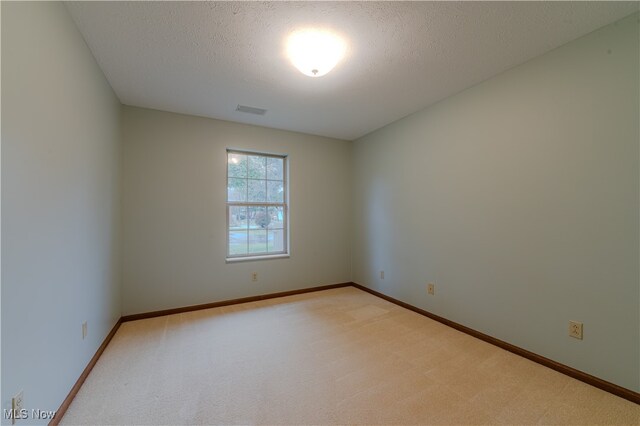 empty room featuring light carpet, a textured ceiling, visible vents, and baseboards