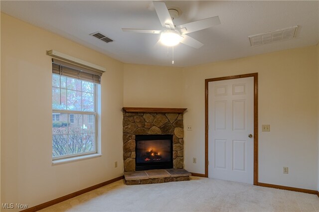 carpeted living area with baseboards, visible vents, a ceiling fan, and a stone fireplace