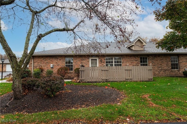 back of property with a yard, roof with shingles, fence, and brick siding