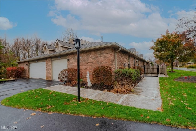 view of side of property featuring a garage, driveway, a lawn, a gate, and brick siding