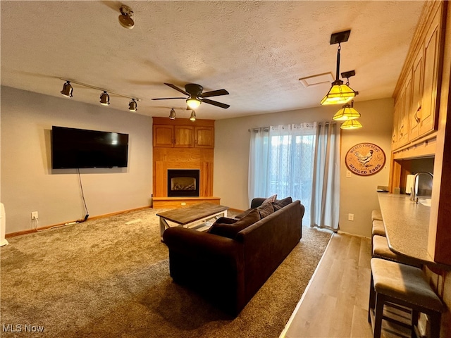 carpeted living room featuring ceiling fan, a fireplace, and a textured ceiling