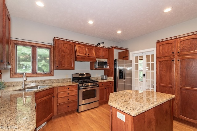 kitchen featuring sink, light stone countertops, light wood-type flooring, a kitchen island, and stainless steel appliances