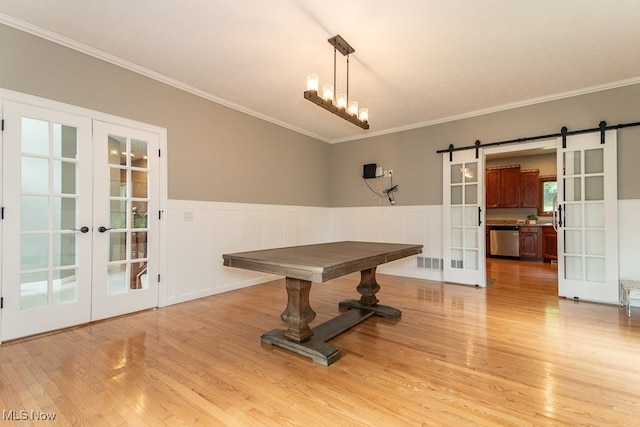 dining room with a barn door, crown molding, light hardwood / wood-style flooring, and french doors