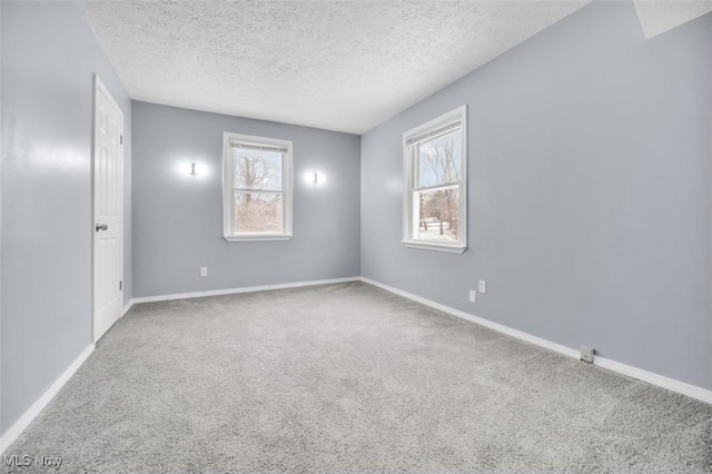 empty room featuring a textured ceiling, carpet flooring, and baseboards