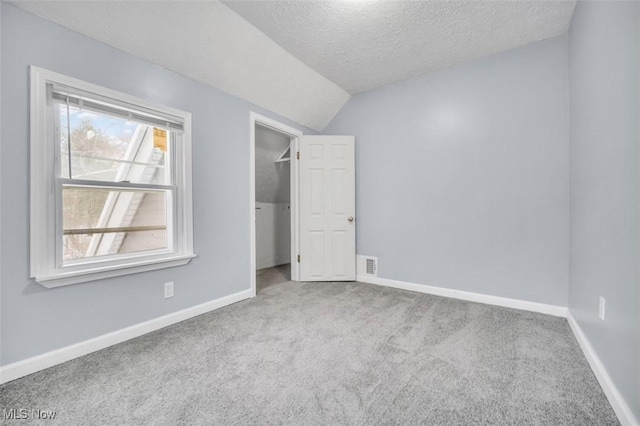 unfurnished bedroom with a textured ceiling, baseboards, a walk in closet, and carpet flooring