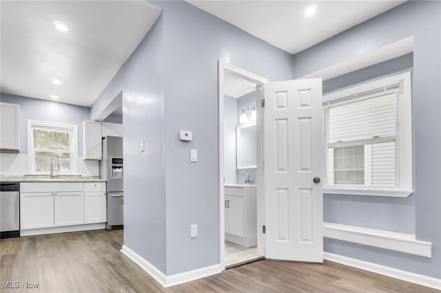 interior space featuring stainless steel appliances, wood finished floors, a sink, baseboards, and white cabinets