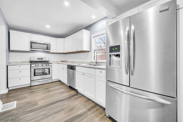 kitchen featuring stainless steel appliances, a sink, white cabinets, light countertops, and light wood-type flooring