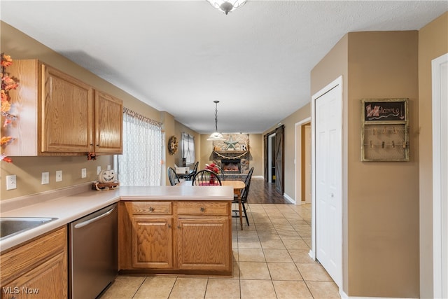 kitchen with kitchen peninsula, stainless steel dishwasher, sink, light tile patterned floors, and hanging light fixtures