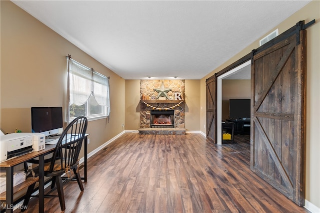 office area featuring a textured ceiling, a fireplace, a barn door, and dark wood-type flooring