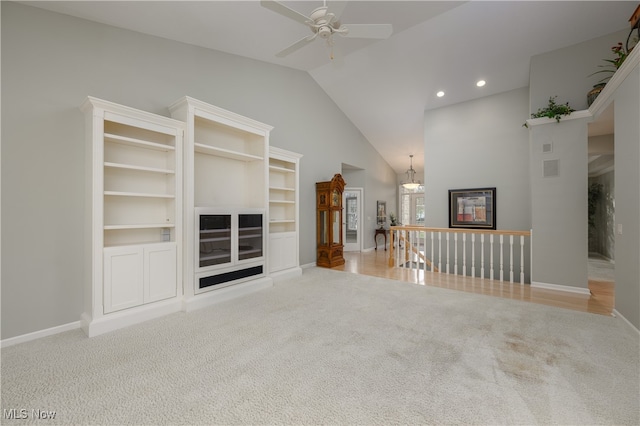 unfurnished living room featuring ceiling fan with notable chandelier, light colored carpet, and high vaulted ceiling