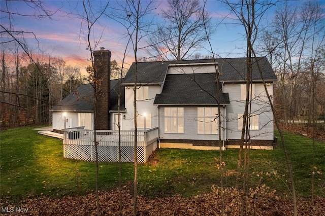 back house at dusk with a lawn and a wooden deck