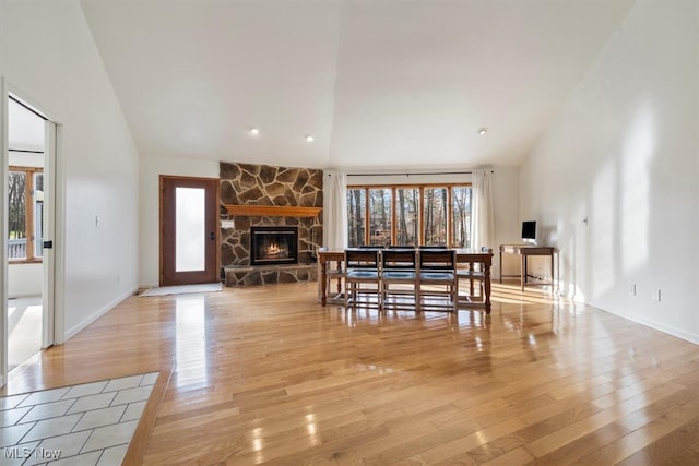 dining room with a stone fireplace, high vaulted ceiling, and light hardwood / wood-style flooring