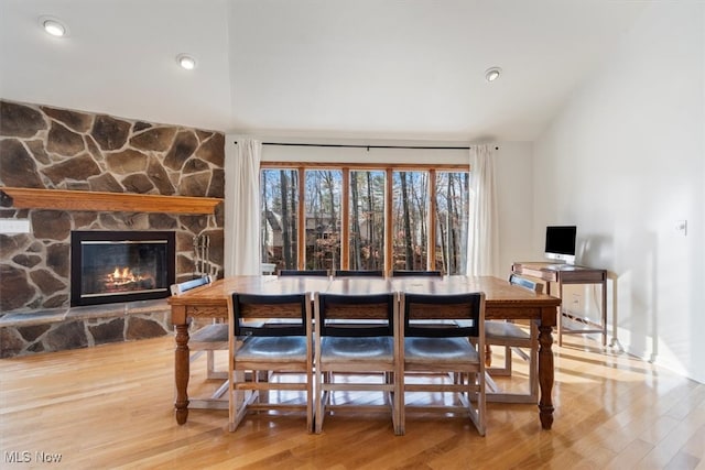 dining space with a stone fireplace, vaulted ceiling, and hardwood / wood-style flooring