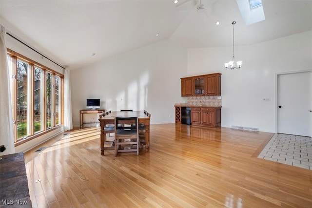 dining area featuring a skylight, light wood-type flooring, high vaulted ceiling, and a chandelier