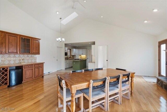 dining room with a skylight, sink, high vaulted ceiling, a chandelier, and light wood-type flooring