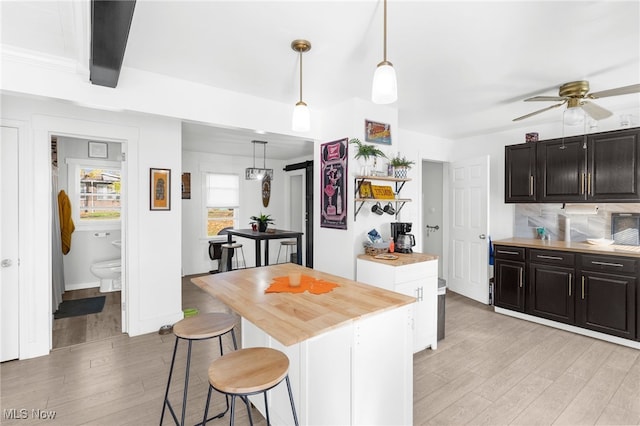 kitchen with a center island, white cabinets, decorative backsplash, light wood-type flooring, and decorative light fixtures