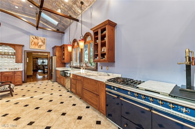 kitchen with a skylight, light stone countertops, hanging light fixtures, high vaulted ceiling, and appliances with stainless steel finishes