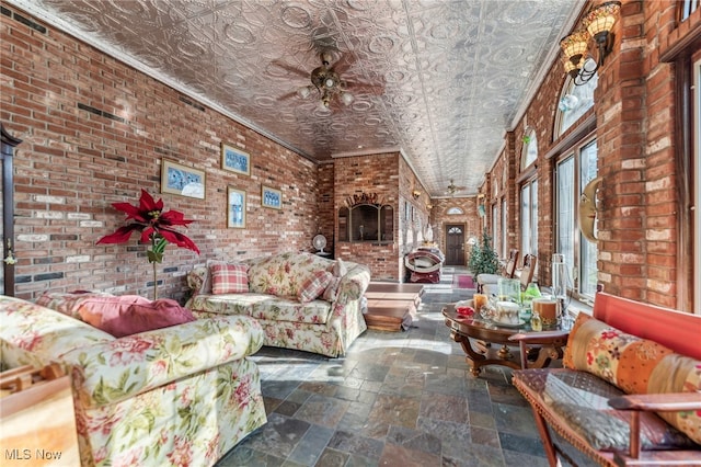 living room with ceiling fan, ornamental molding, and brick wall