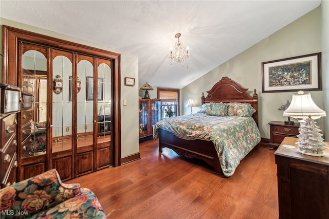 bedroom with hardwood / wood-style floors, an inviting chandelier, and vaulted ceiling