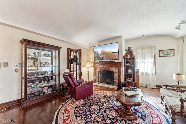 living room with a fireplace, a textured ceiling, dark hardwood / wood-style floors, and vaulted ceiling